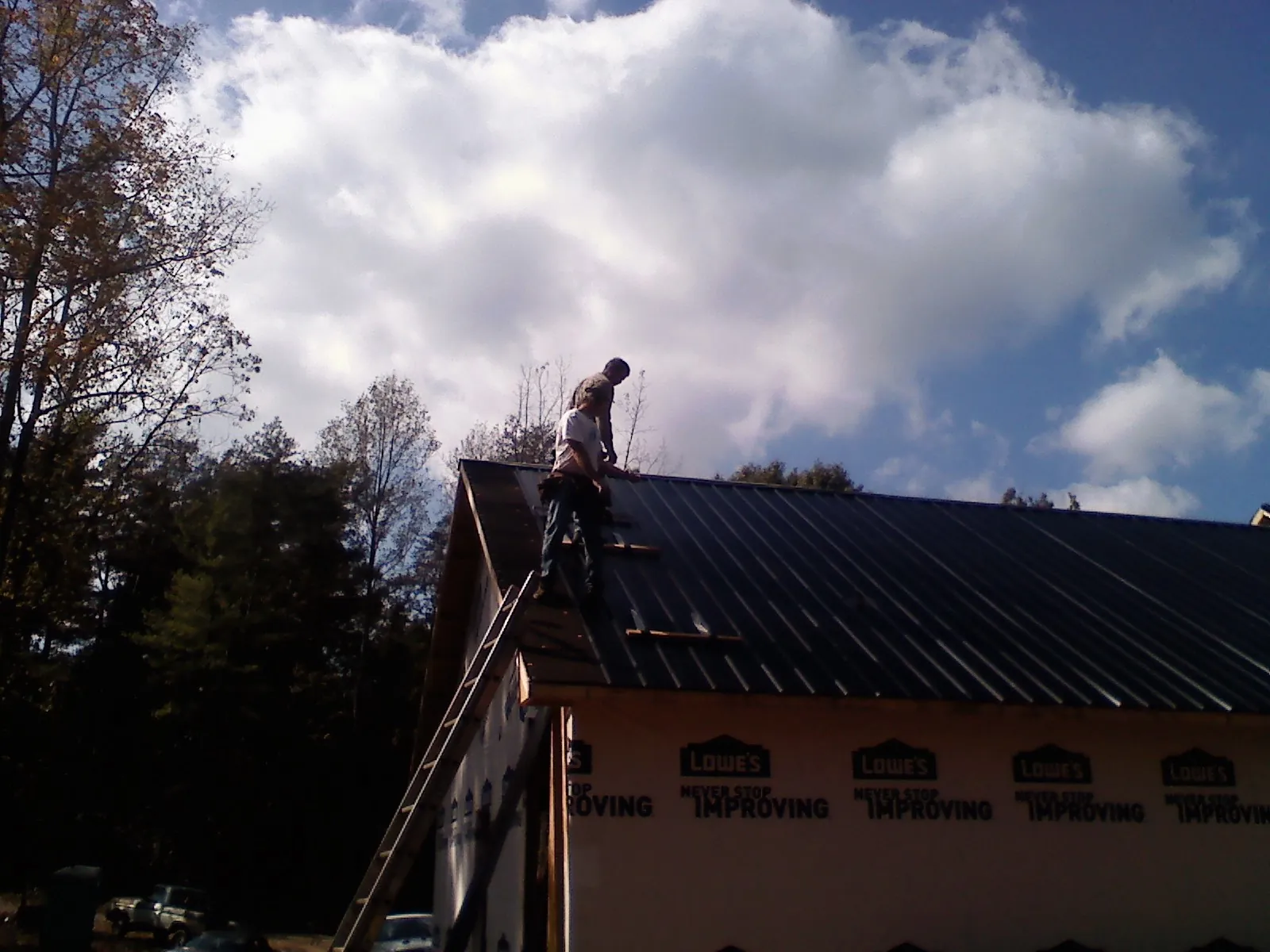 Roofer fastening dark metal panels high against a cloudy sky, from a Roof Inspection job in Westlake