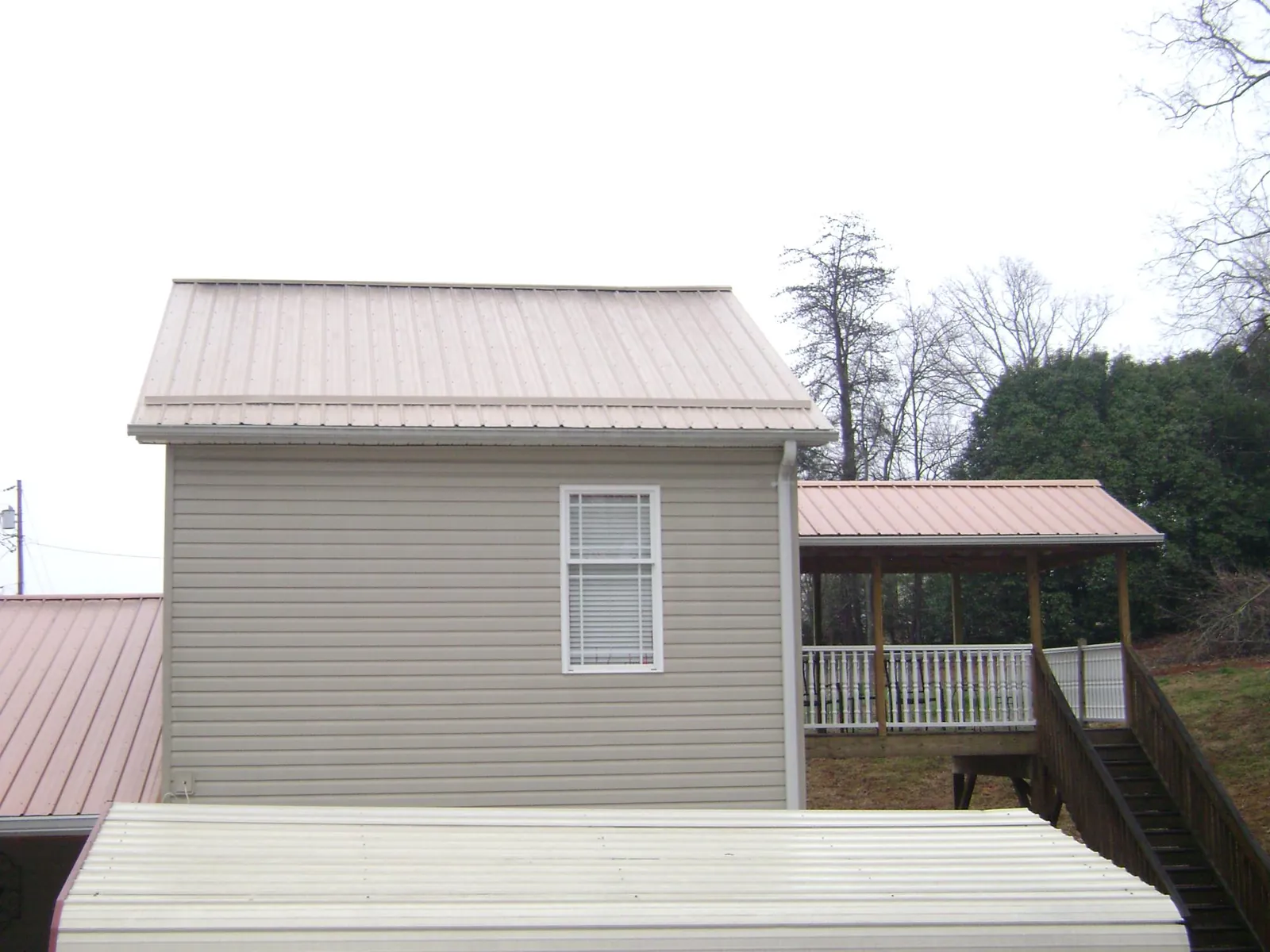 Tan metal roofs on a two story addition and attached porch, from a Roof Replacement job in Westlake